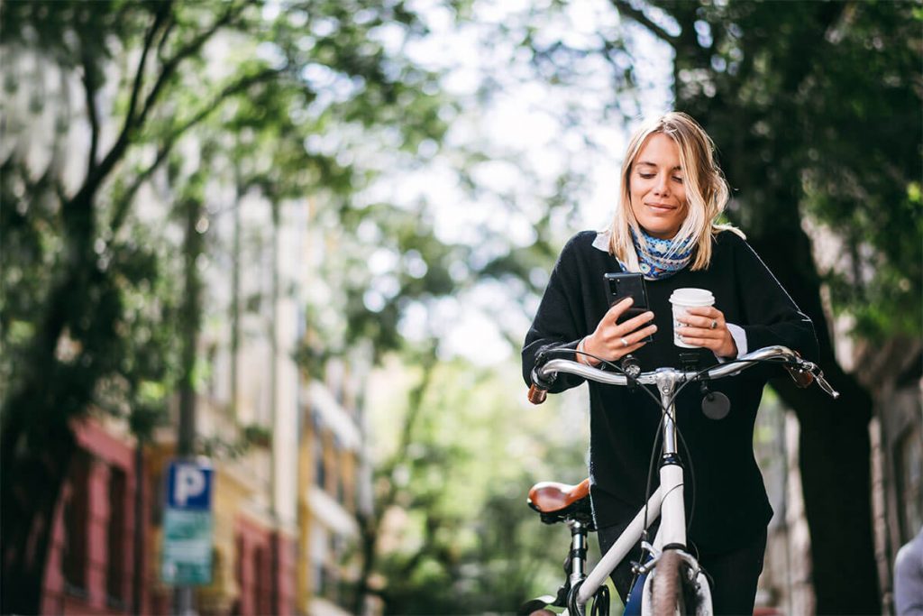 lächelnde Frau an einem Smartphone auf einem Fahrrad
