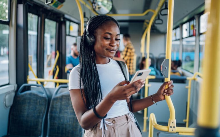 Junge Frau schaut auf ihr Handy im Bus und lächelt
