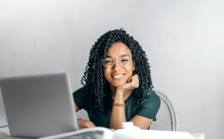 Junge Frau mit dunklen lockigen Haaren sitzt lächelnd vor ihrem Laptop