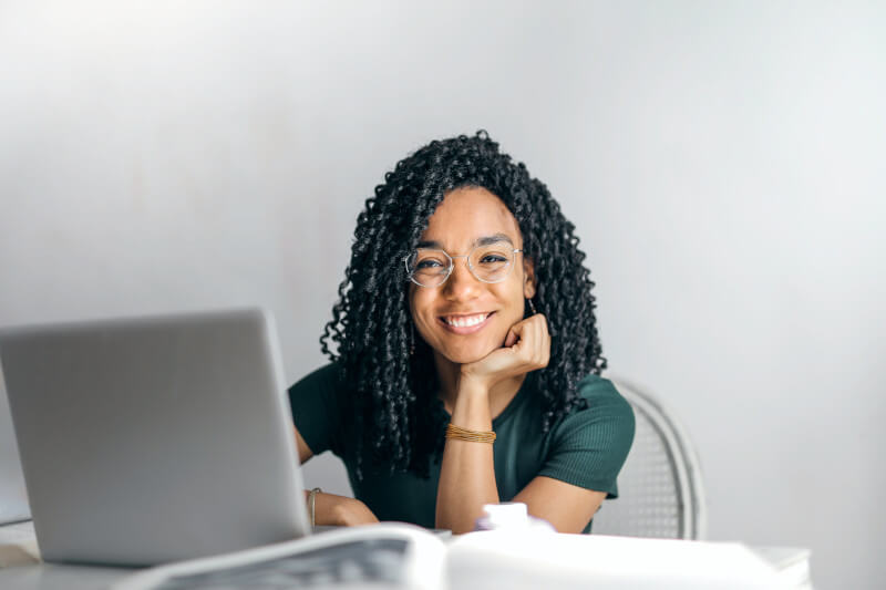 Junge Frau mit dunklen lockigen Haaren sitzt lächelnd vor ihrem Laptop