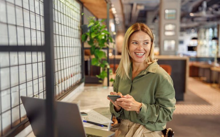 Lächelnde Frau im Büro mit Handy und Laptop