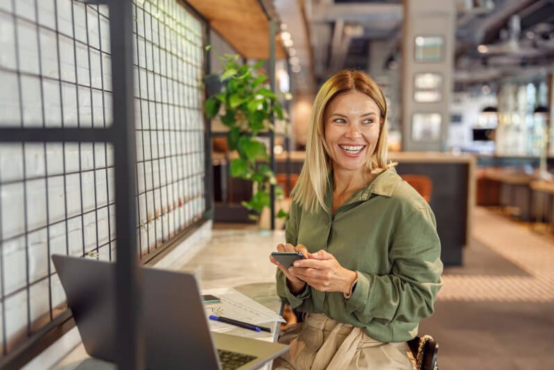 Lächelnde Frau im Büro mit Handy und Laptop