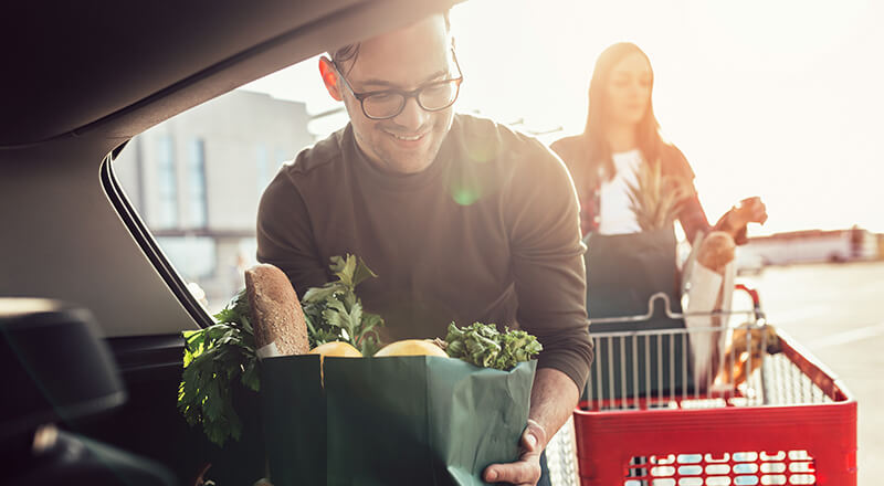 Mann und Frau beim Einladen von Lebensmitteln in den Kofferraum eines Autos