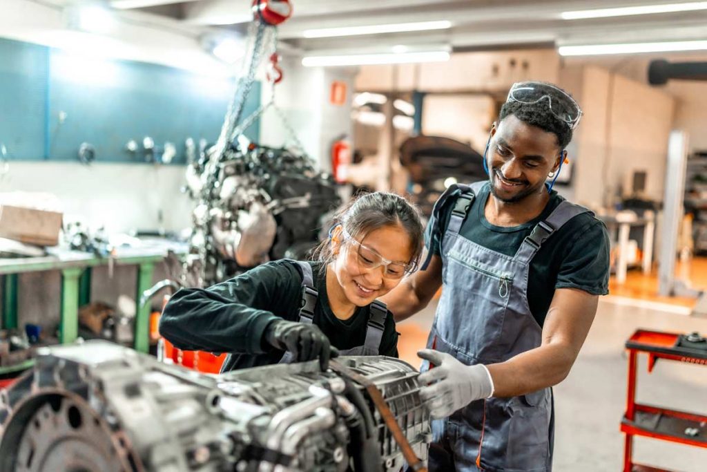Zwei glückliche KFZ-Mechatroniker arbeiten zusammen an einem Motor