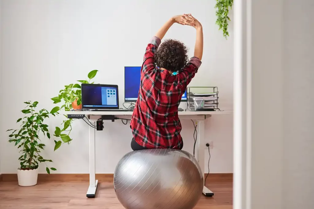 Frau auf einem Gesundheitsball streckt sich an ihrem ergonomischen Arbeitsplatz aus