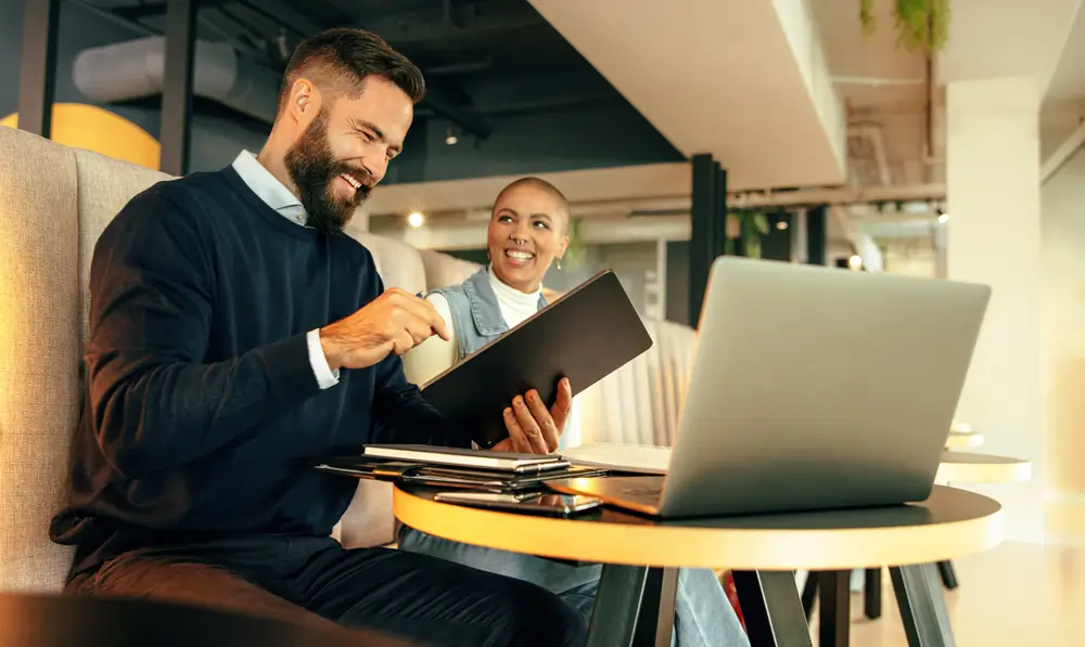 Ein Mann und eine Frau sitzen im Office vor ihrem Bildschrim und freuen sich über ihre Zusatzleistung vom Arbeitgeber